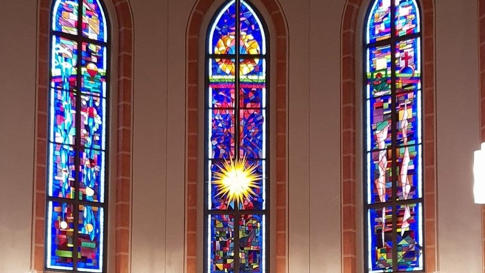 Drei bunte Kirchenfenster mit religiösen Motiven