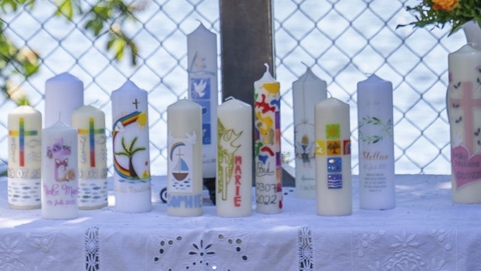 Ein Tisch mit weißer Tischdecke, darauf ein großes Holzkreuz und mehrere Kerzen in verschiedenen Farben