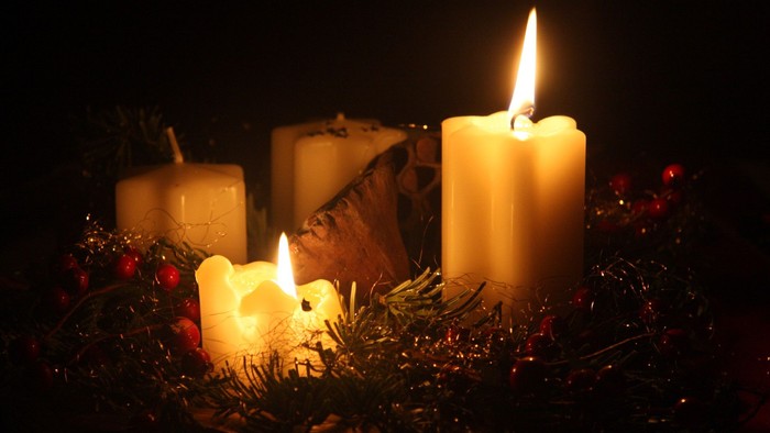 Drei brennende Kerzen in Adventskranz mit Tannenzweigen und Beeren