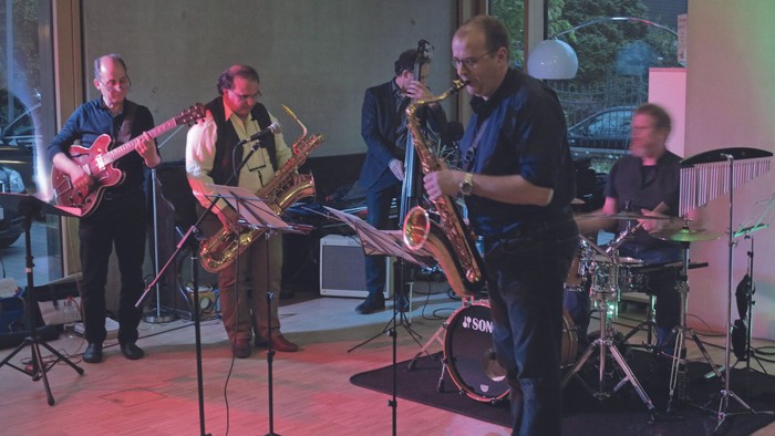 Eine Band spielt auf einer Bühne, Musiker mit Saxophon, Gitarre und Schlagzeug