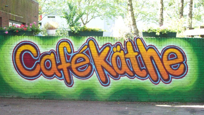 Farbenfrohes Graffiti "Cafe Kathe" an grünem Ziegelmauerwerk