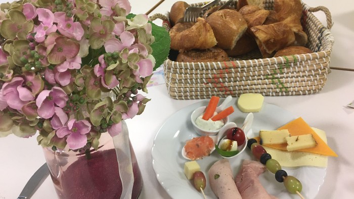 Blumenstrauß, Brotkorb und Platte mit Aufschnitt und Gemüse