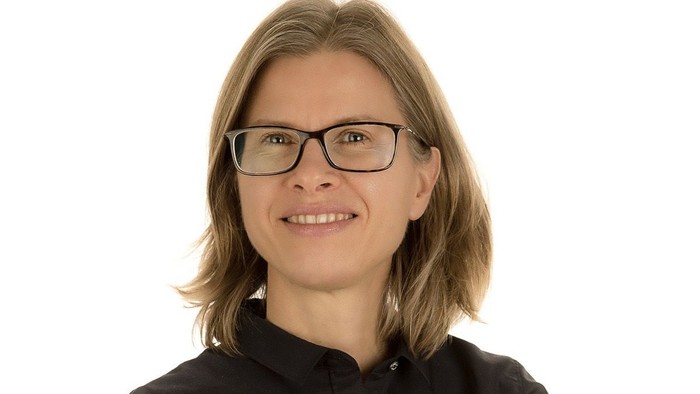 En kvinde med kort hår og briller, smiler til kameraet.