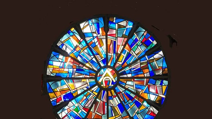 Buntes, kreisförmiges Mosaikfenster mit zentralem Symbol.