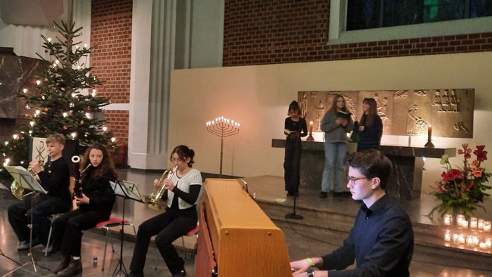 Eine Gruppe von Menschen singt Weihnachtslieder in einem Raum mit Weihnachtsbaum und Kerzen.