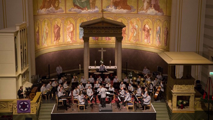 Eine große Gruppe von Menschen versammelt sich in einer prächtigen Kirche, viele sitzen, einige stehen, vor einem Altar.