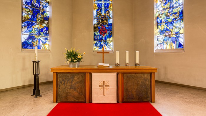 Ein Altar in einer Kirche mit farbenfrohen Buntglasfenstern und Kerzen.