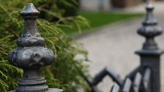 En smuk og detaljeret svart jernstaket med blomsterformet top, placeret ved en grøn og velholdt have.