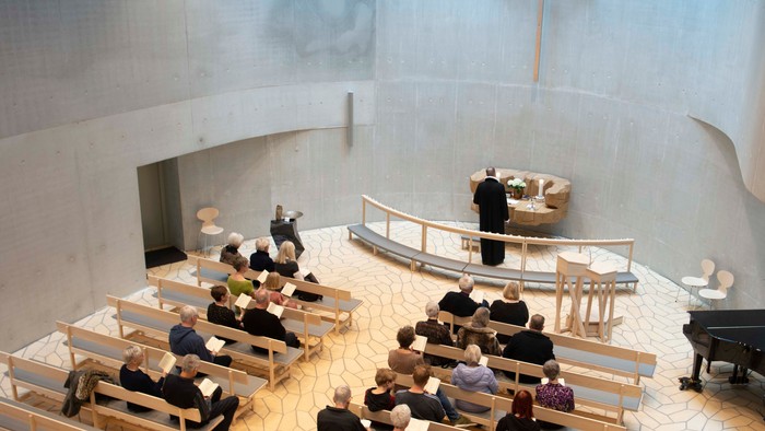 En moderne kirke med folk, der sidder på benker og en præst ved alteret