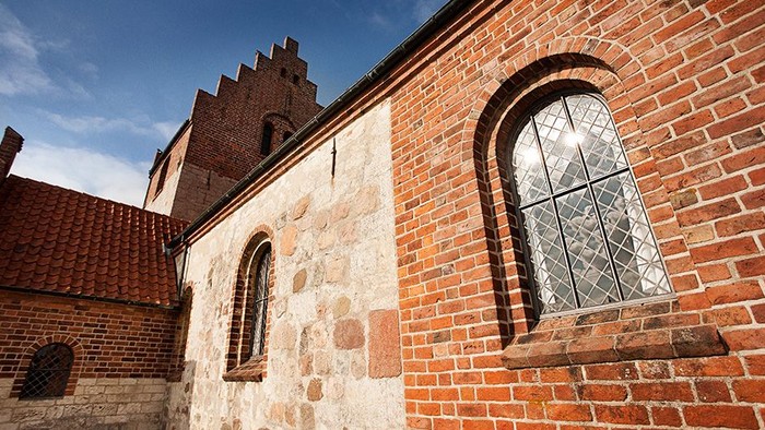 Det er et billede af en mur af røde mursten med et vindue og en tårn i baggrunden