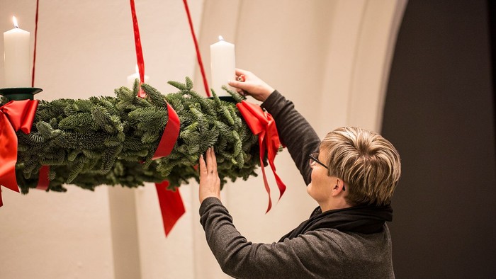 Kvinde hænger en julekrans med lys og røde bånd op på væggen