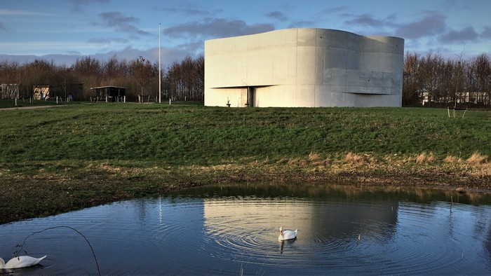 En lang, lav bygning ved en sø med svane i forgrunden