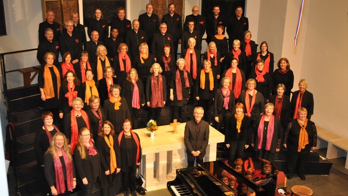 Große Gruppe von Menschen in Kirchenraum, viele mit roten Schals, vor Klavier und Schlagzeug posierend