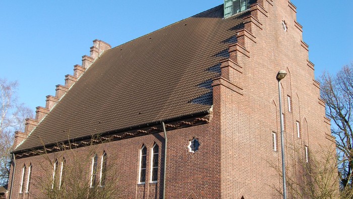 Kirchengebäude mit hohem Turm und spitzem Dach an der Straße
