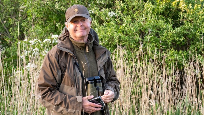 En person står i en naturlig omgivelse og holder binokler.
