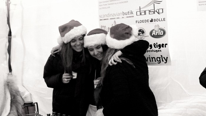 Tre kvinder i julehatter danser og smiler på fest.