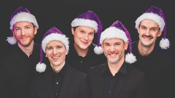 Fünf Männer in schwarzen Anzügen und Weihnachtsmützen lächeln.
