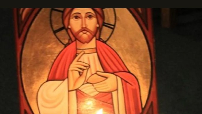 En lysstake med lys foran et billede af Jesus