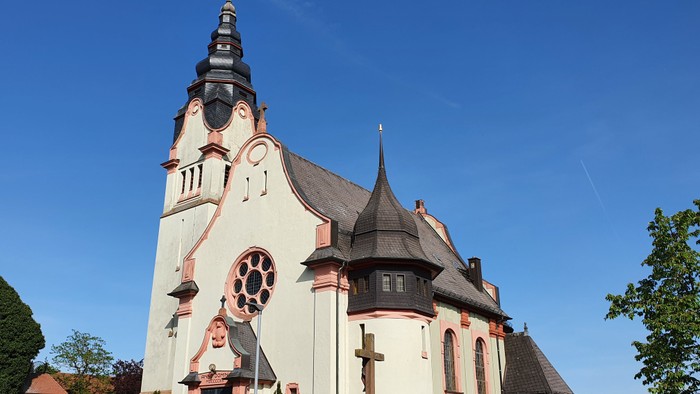 Die Kirche hat einen hohen Turm und ein rosafarbenes Kreuz.