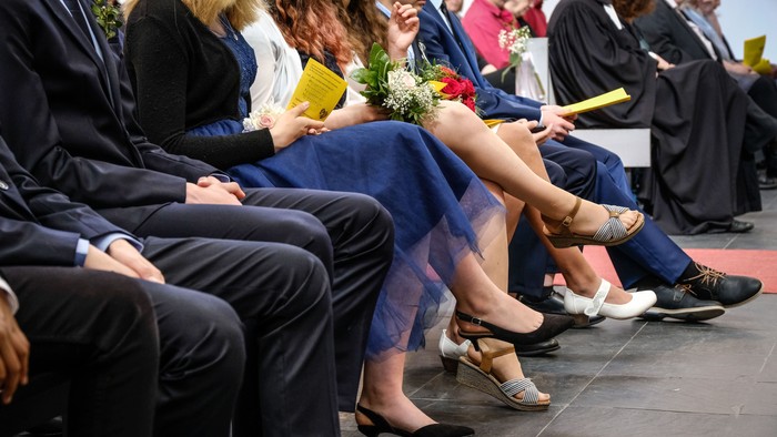 Eine Gruppe von Menschen sitzt in einer Reihe, einige lachen und halten Blumen.