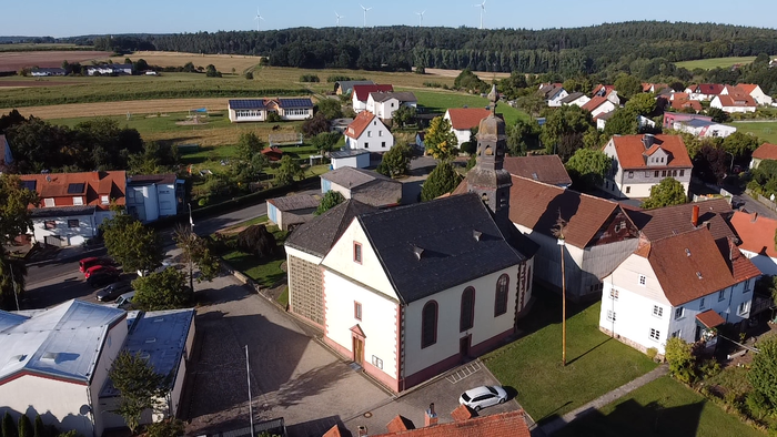 Dorf mit Kirche und umliegenden Häusern, umgeben von Feldern und Wäldern
