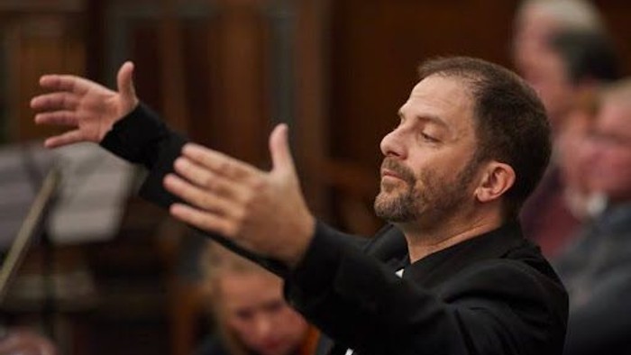 En mand dirigerer et orkester med udstrakt arme.