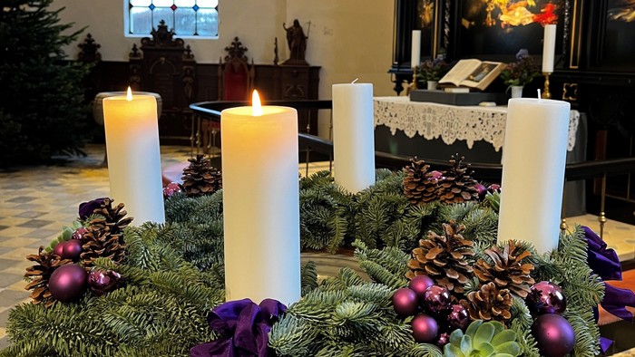 En adventskranse med lys og grønne blomster i kirke.