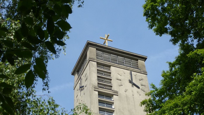Der Turm einer Kirche ragt zwischen Bäumen empor