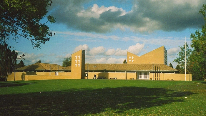 Et stort, gult bygning på grønne areal med træer og en blå himmel.