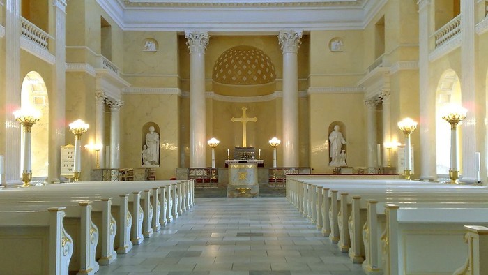 Indre del af en stor, lys og pompøs kirke med høje kolonner og lysende lys.