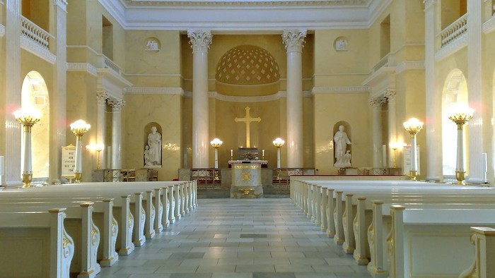 Indre del af en stor, lys og pompøs kirke med høje kolonner og lysende lys.