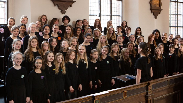 En stor kor, der består af både voksne og børn, poserer sammen i en kirke.
