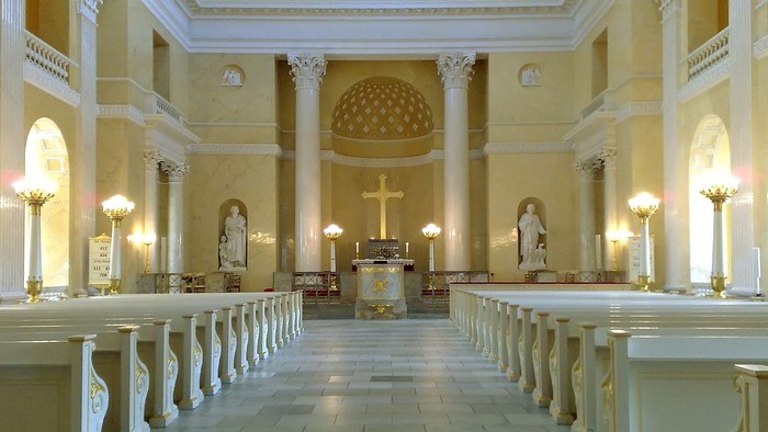 Indre del af en stor, lys og pompøs kirke med høje kolonner og lysende lys.