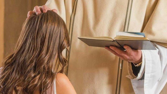 En præst udfører en religiøs ritual med en ung pige i kirken.