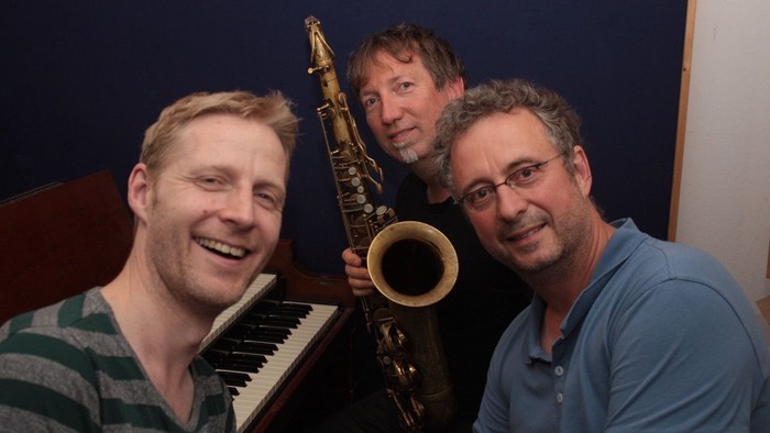 Drei Männer posieren mit Musikinstrumenten in einem Studio