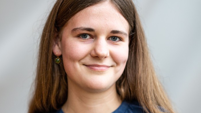 En ung pige med lang, blond hår, smilende og børne, og blå bluse.