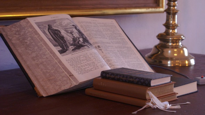 En åben bog, en lille boksamling og en gylden lampestativ på en skrivebord