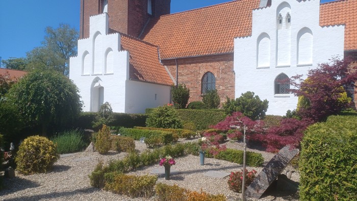 En smuk kirke med røde tag og hvidt udseende, omgivet af en fin have med blomster og buske