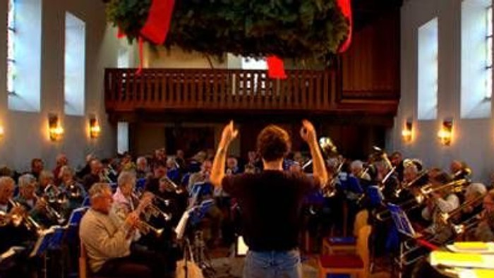 Ein Orchester probt in einem großen Saal unter der Leitung eines Dirigenten.