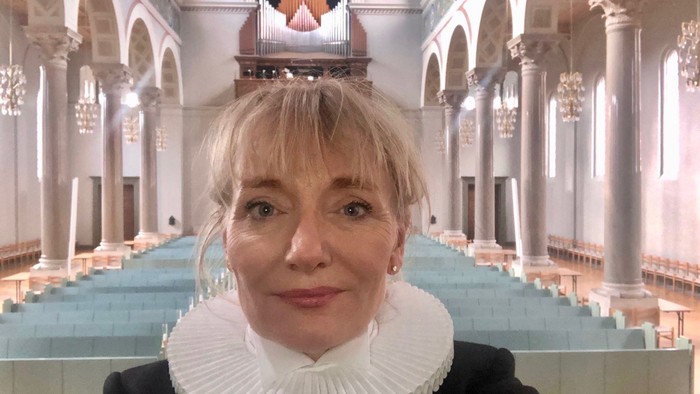 Kvinde med hvid krage står i stor kirke med orgel.
