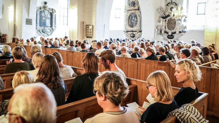 En kirkefuld af mennesker, der deltager i en gudstjeneste.