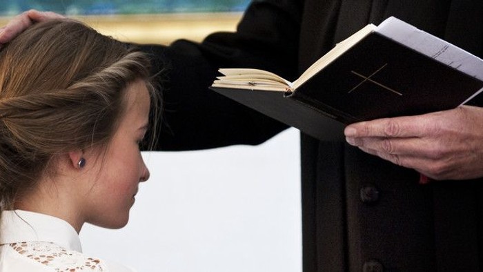 En ung pige ser på en bog, som en mand i mørkt kostume holder op for hende