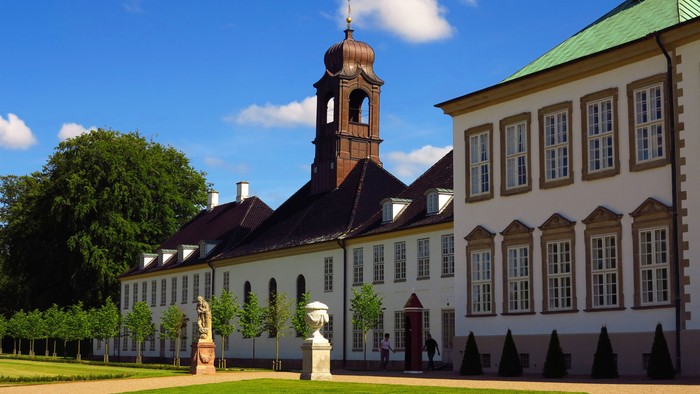 Stor, hvid palækompleks med klokketårn og grønne arealer