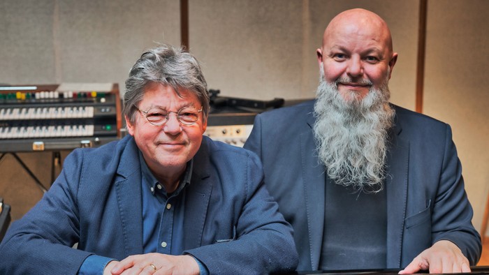 To børn med briller og skæg sitter ved piano