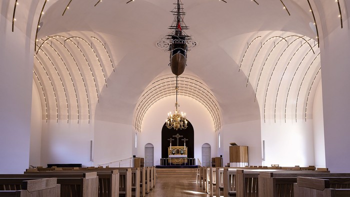 Indre del af en stor, belyset kirke med høje buer og træbænke.