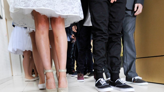 En brud og to mænd står sammen, deres ben synes. Bruden bærer hvide high heels, en mand sort sko og den anden grå sko.