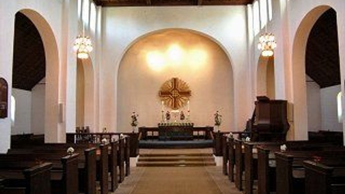 En indre del af en kirke med bænke, alter og lys.