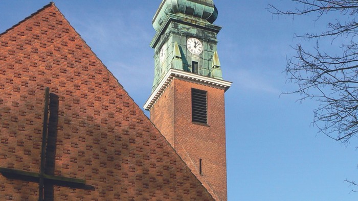 Kirchturm mit Uhr und Kreuz am Gebäude