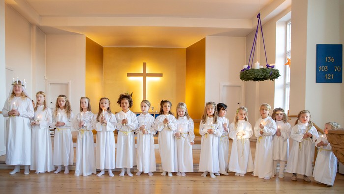 En gruppe børn i hvide tøjer står i en kirke foran et kors