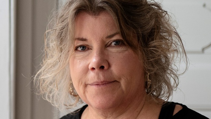 En kvinde med kort, krøllet hår og en sort trøje står foran en hvid dør.